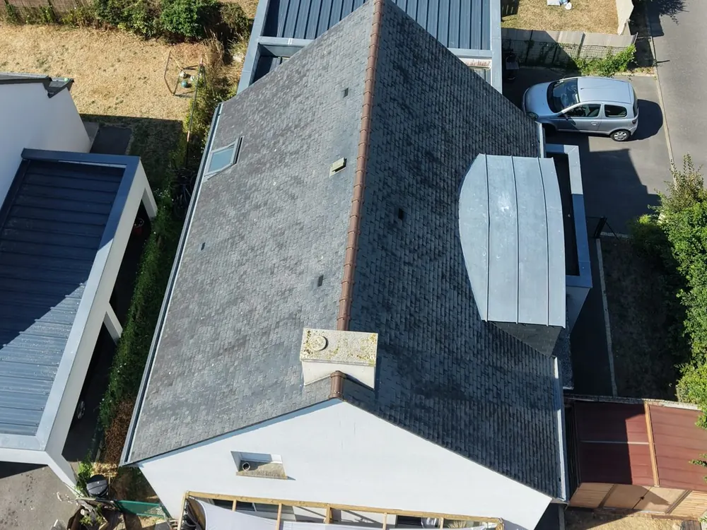 Vue aérienne verticale d'une toiture en ardoise avec cheminée et lucarne