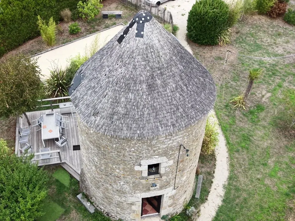 Vue aérienne d'une tour en pierre et de son annexe en bois, entourées d'un jardin